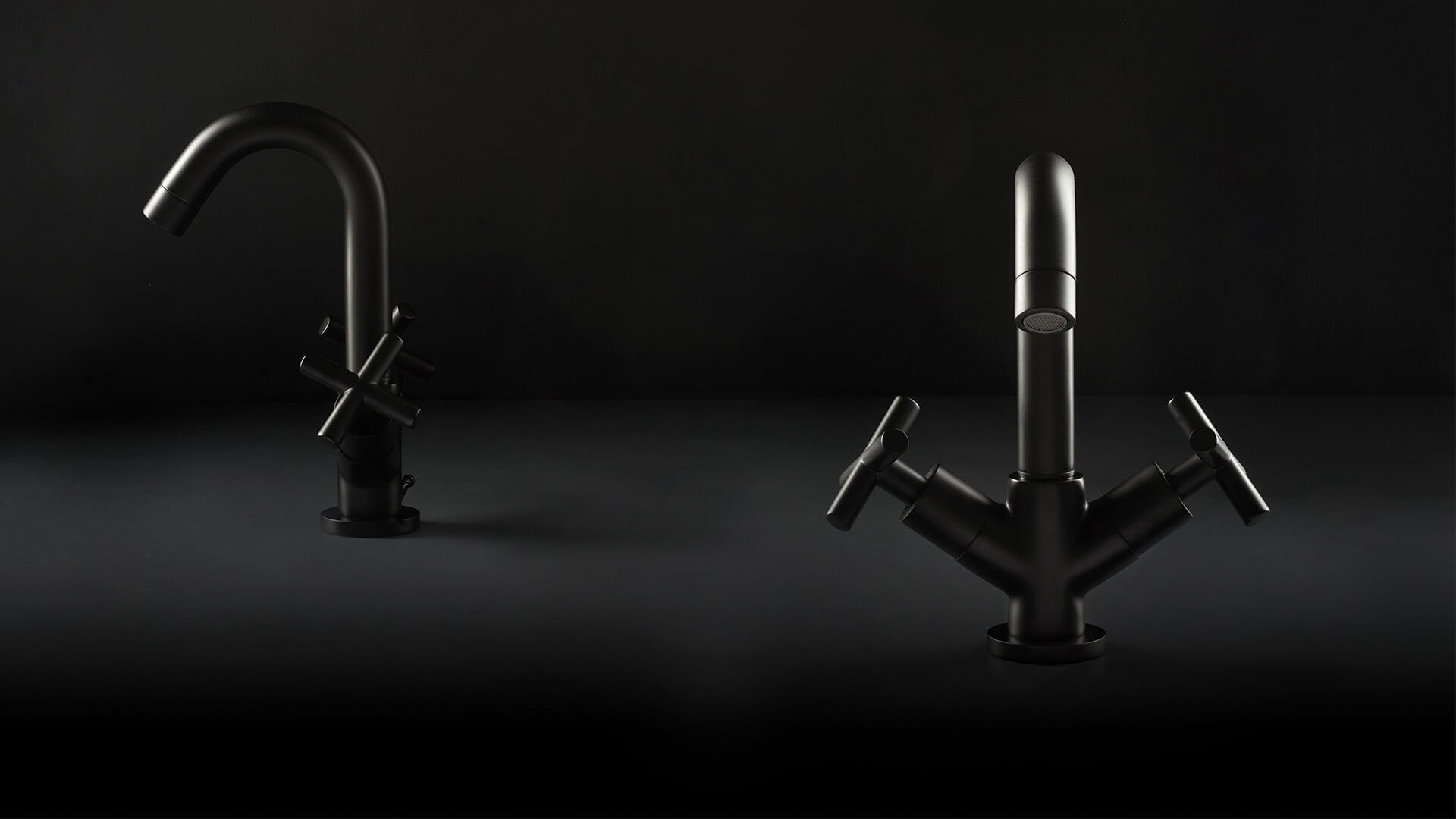 Dos grifos metálicos oscuros sobre un fondo oscuro, uno con caño curvo y el otro con manijas en cruz.