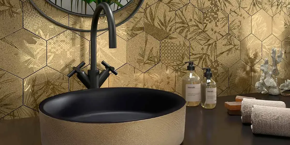 Baño con pared de azulejos hexagonales dorados, lavabo y grifo negros y artículos de tocador.