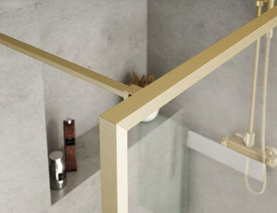 Detalle de esquina de mampara de ducha con marco dorado contra una pared gris texturizada, con un estante incorporado que contiene dos artículos de tocador.