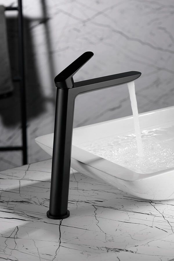 Grifo negro que vierte agua en un lavabo blanco, sobre un fondo de mármol.