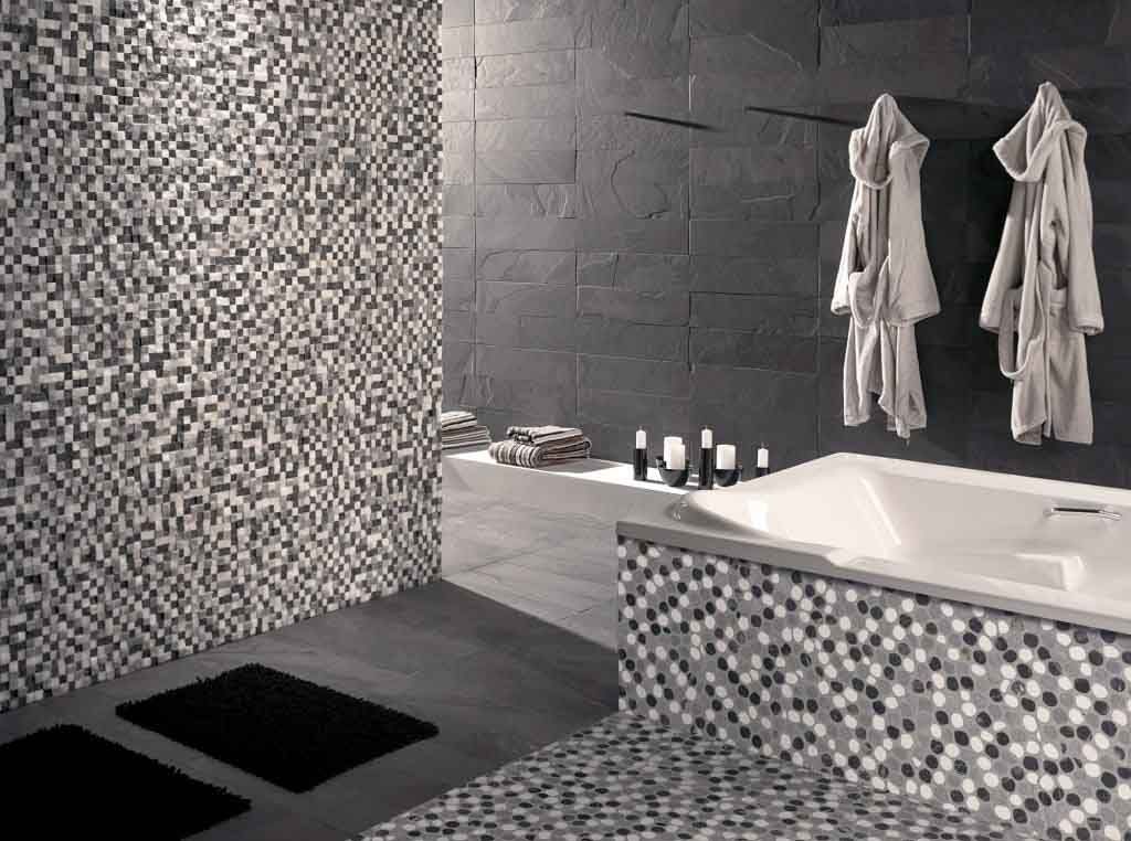 Baño monocromático con mosaicos, bañera, albornoces y pared de piedra oscura.