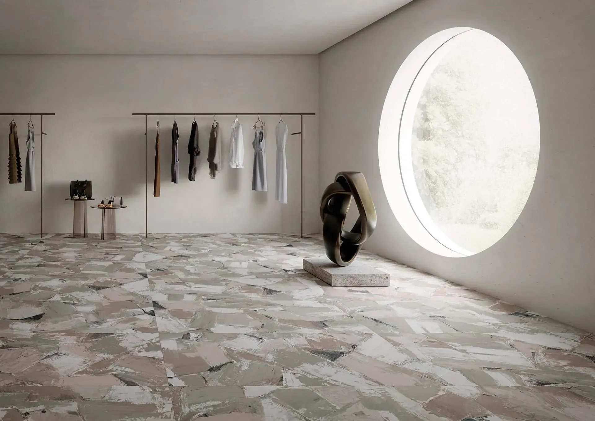 Interior de tienda de ropa minimalista con prendas colgadas, esculturas y una ventana redonda.