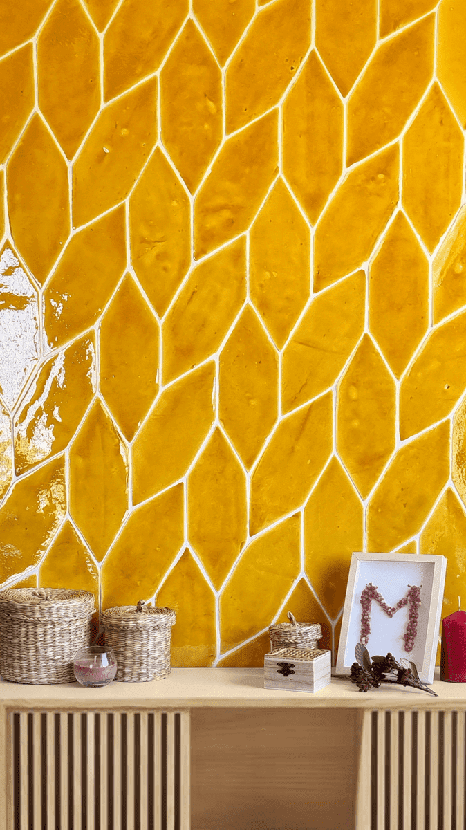 Pared de azulejos con diseño de diamantes amarillos con estante decorativo que sostiene cestas, arte enmarcado y una vela.