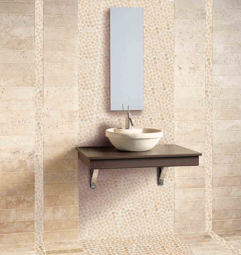 Baño con azulejos color crema y una pared con detalles de piedra. Un lavabo blanco se encuentra sobre una repisa de madera oscura bajo un espejo.