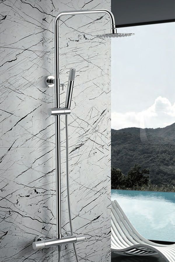 Artefacto de ducha cromado sobre pared de mármol con vista exterior a piscina y montañas.