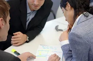 Tres personas vestidas de negocios examinando un documento en una mesa, resaltando con un marcador.