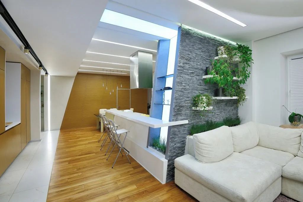 Moderna sala de estar con pisos de madera, sofá seccional blanco y una pared verde con plantas.