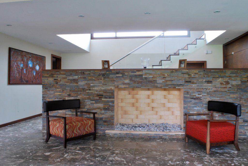 Dos sillones frente a una chimenea de piedra en un interior moderno, con escaleras y un tragaluz visibles.