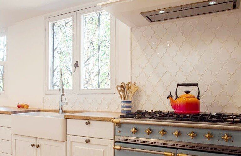 Cocina con gabinetes blancos, fregadero estilo granja, estufa azul y tetera naranja.