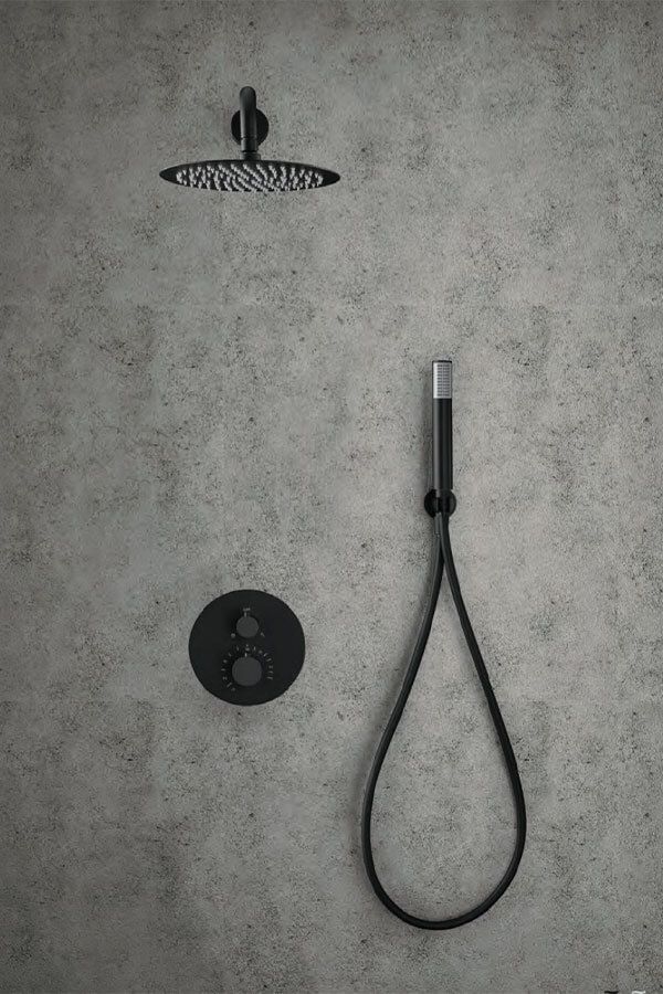 Ducha negra sobre pared de hormigón gris. Incluye cabezal de ducha, rociador de mano y mando de control.