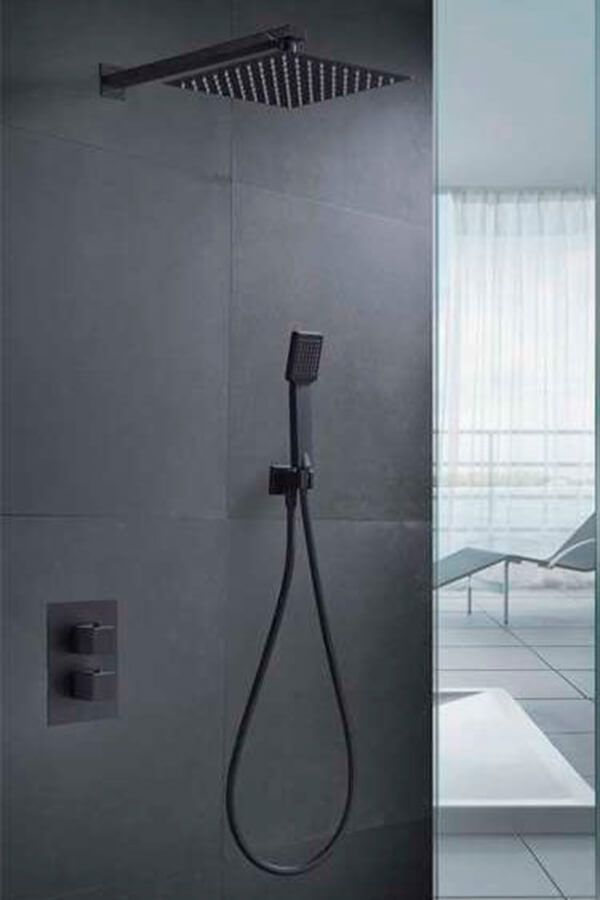 Cabezal de ducha negro y accesorios de ducha de mano sobre una pared de azulejos de color gris oscuro.