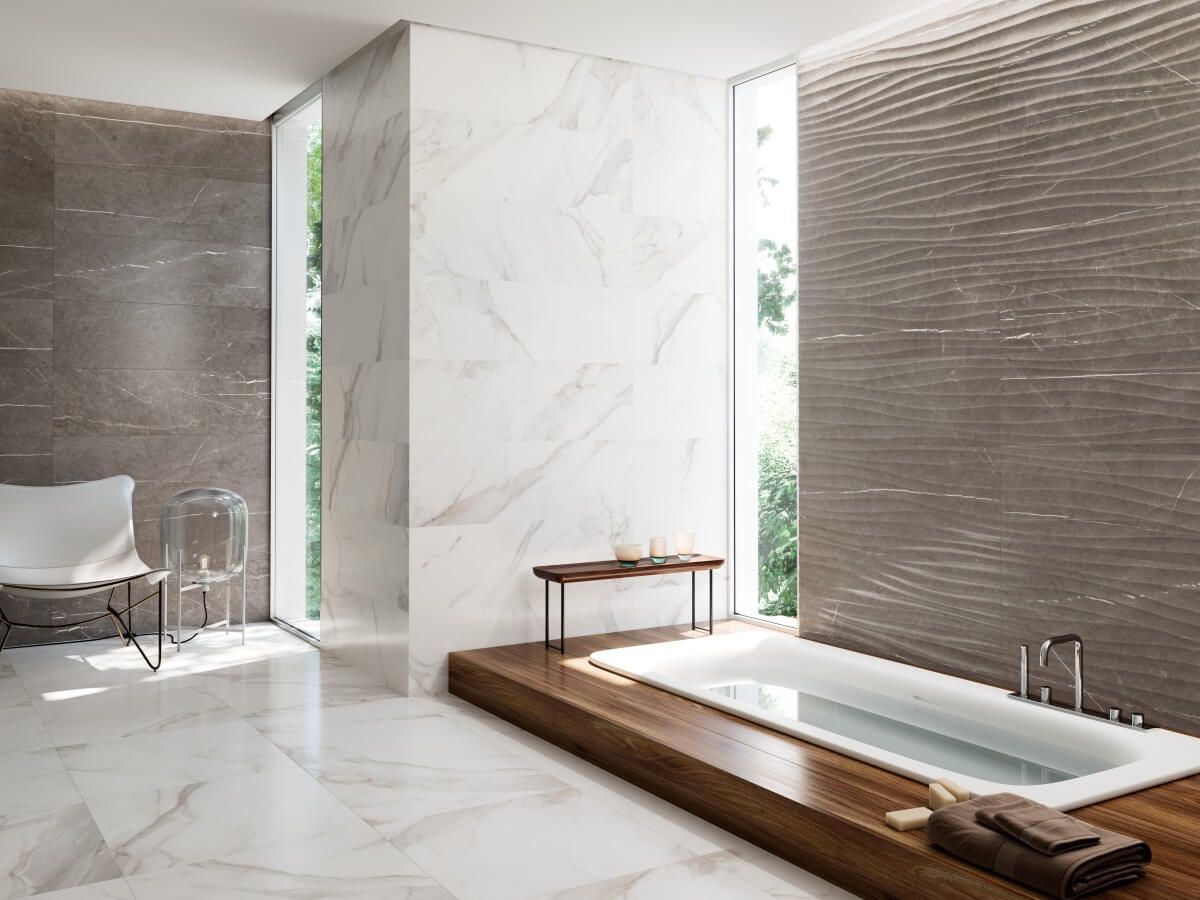 Baño moderno con detalles de mármol y madera, ventanas grandes y una bañera profunda.