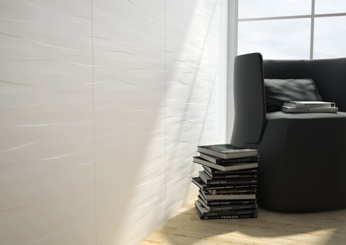 Pared texturizada blanca, sillón negro, pila de libros y luz solar entrando por una ventana.