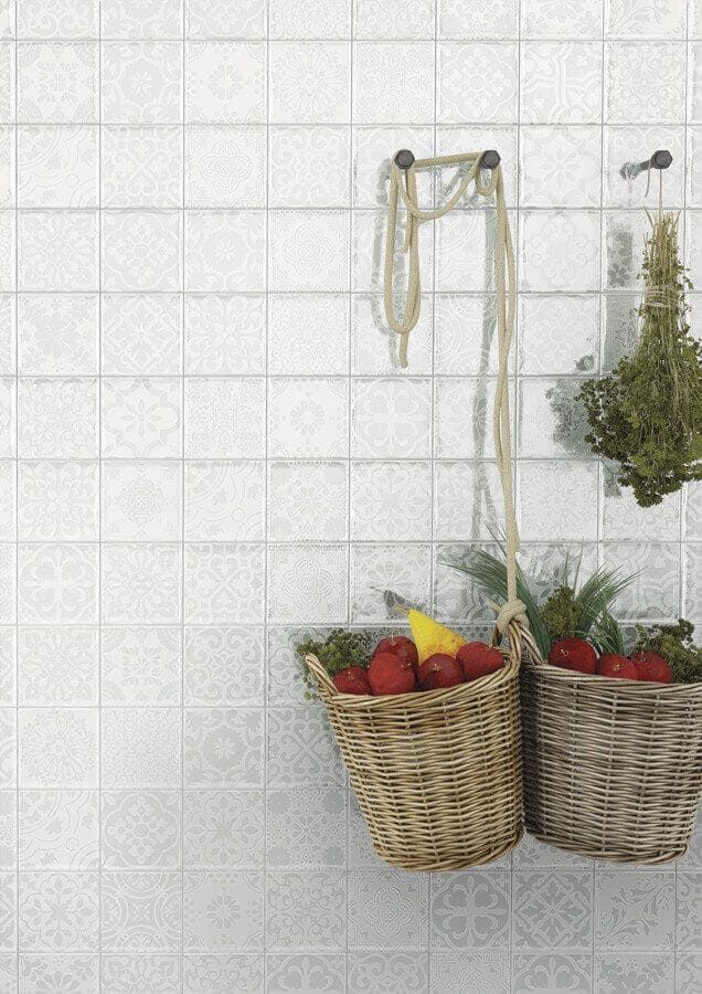 Pared de azulejos blancos con cestas de frutas y hierbas colgando de ganchos.