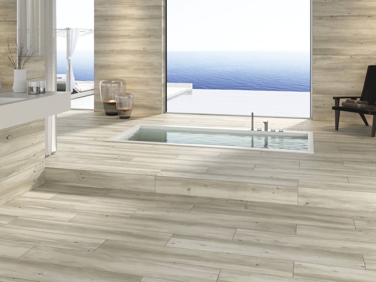 Baño con azulejos imitación madera, bañera incorporada y vista al mar desde un gran ventanal.