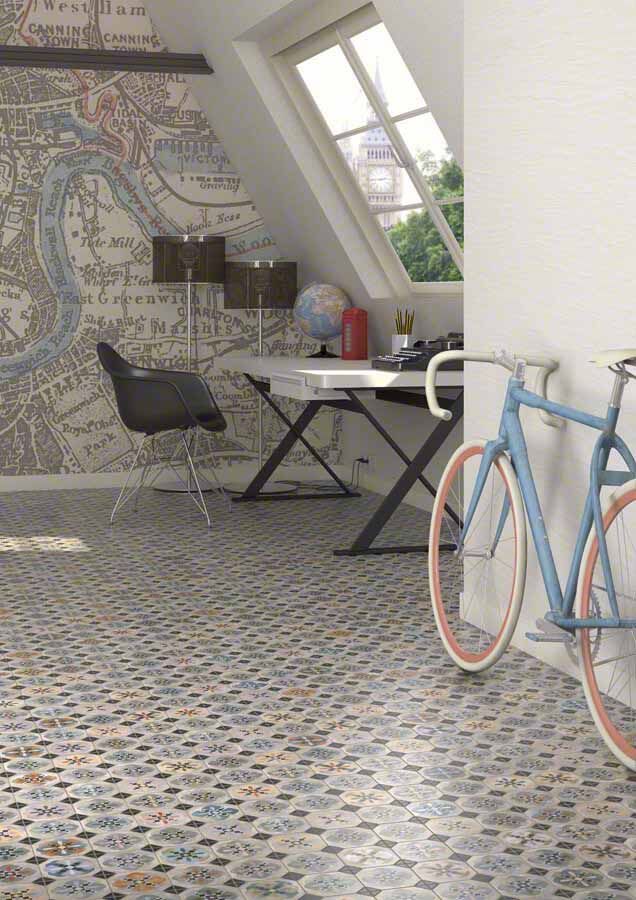 Habitación abuhardillada con una bicicleta azul, un escritorio y un papel pintado con un mapa. Suelo con estampado de rombos.
