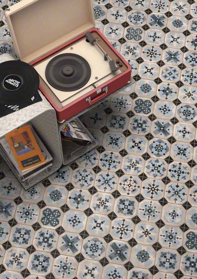 Tocadiscos rojo sobre suelo de baldosas estampadas en azul y blanco con discos de vinilo.