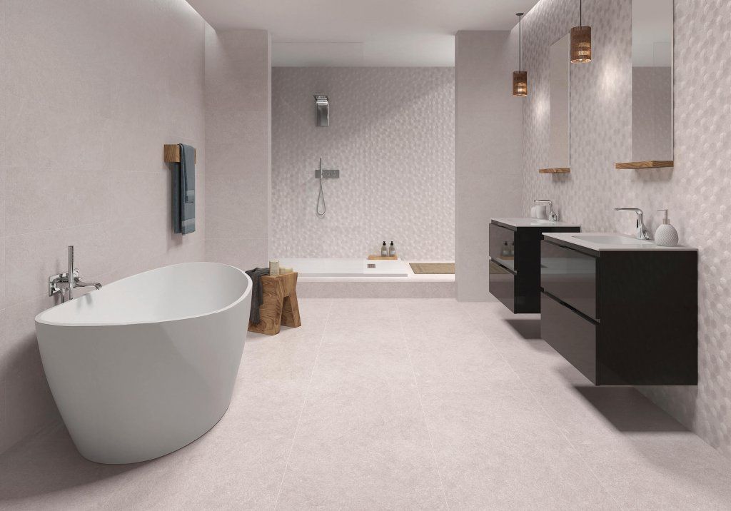 Baño moderno con bañera blanca, tocadores negros, paredes de color rosa claro y azulejos texturizados.