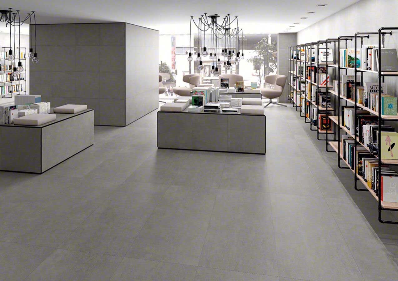 Interior de librería moderna con tonos grises; estanterías, mesas de exhibición y zona de estar.