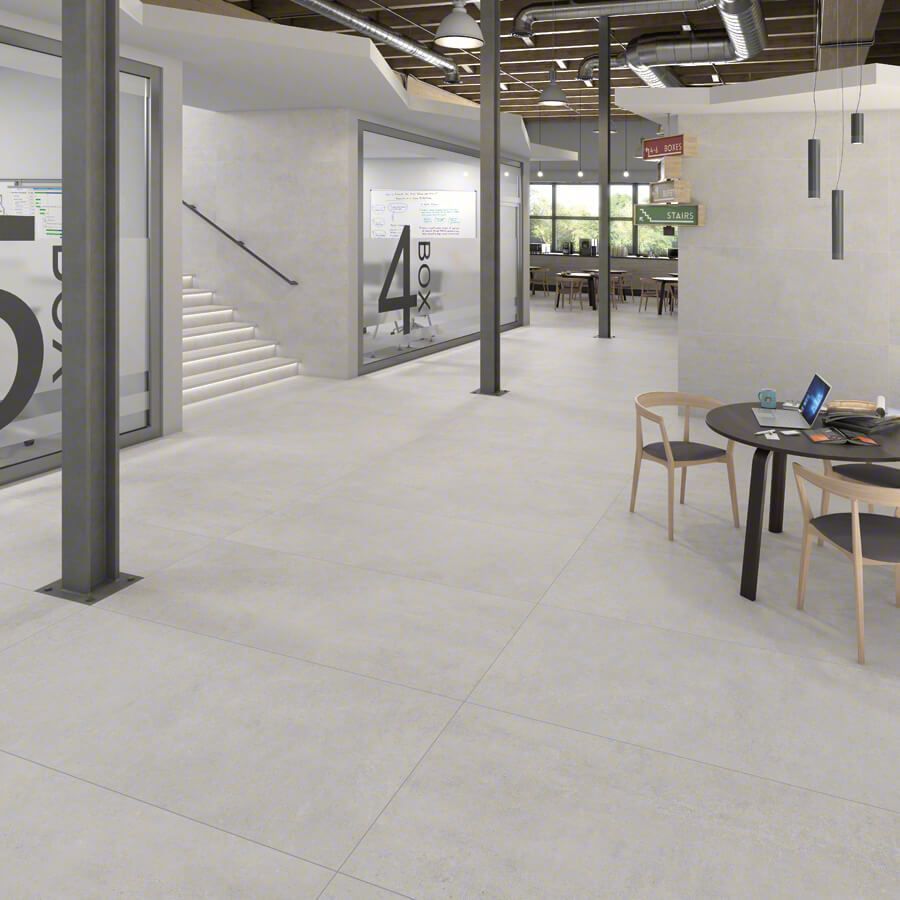 Lobby de oficina moderno con pisos de colores claros, columnas, escaleras y una mesa redonda con sillas.