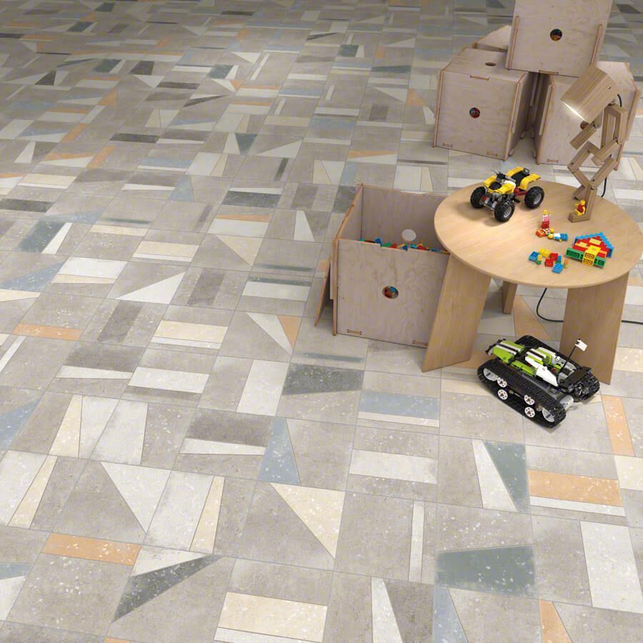 Suelo de sala de juegos con baldosas geométricas de colores; juguetes sobre una mesa y suelo, cajas de cartón.