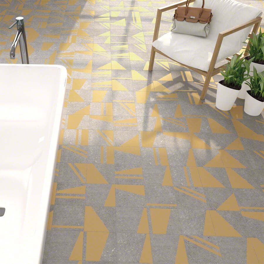 Baño con azulejos con estampados grises y detalles amarillos; silla, bañera y plantas.