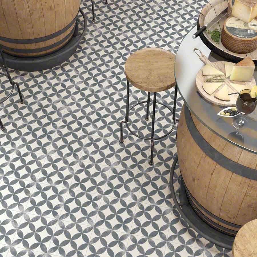 Piso con diseño de azulejos azules y blancos, mesas de barril de madera, taburete y presentación de quesos y vinos.