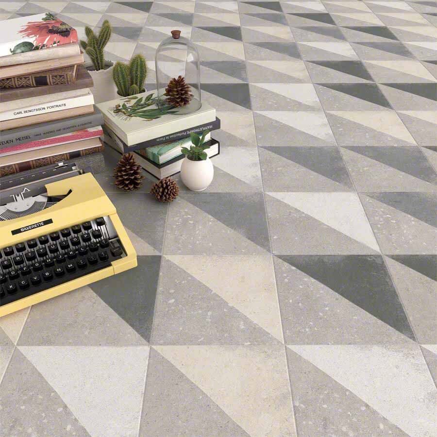 Máquina de escribir amarilla y libros sobre un piso de baldosas con dibujos geométricos con triángulos grises y blancos.