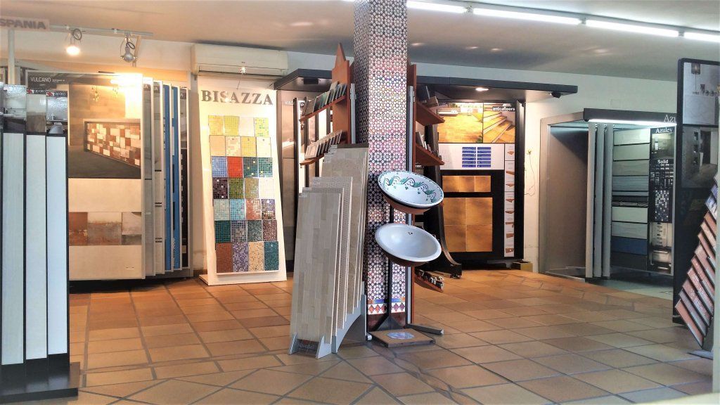 Interior de una sala de exposición de azulejos con expositores y detalles decorativos. Suelo marrón e iluminación brillante.