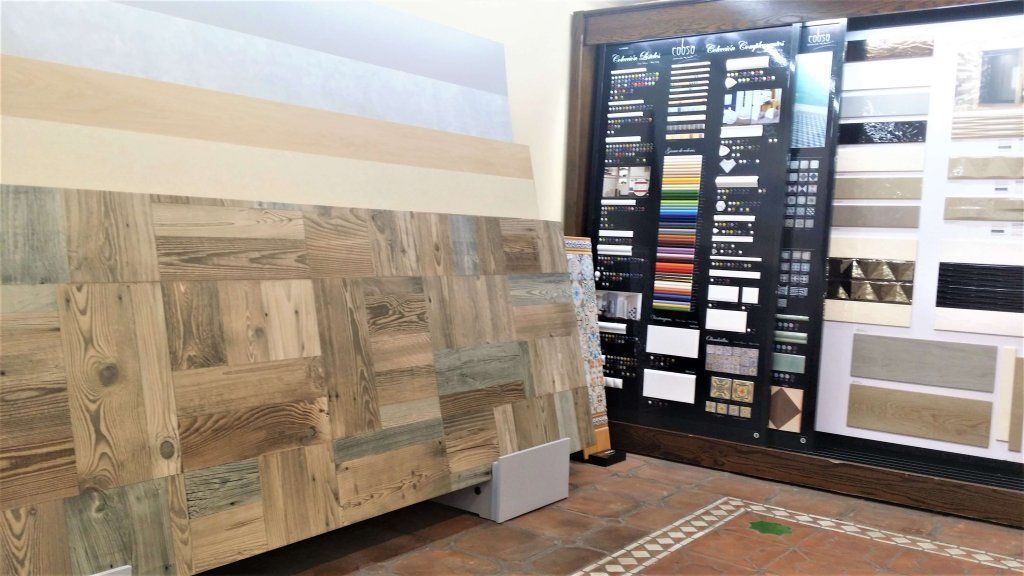 Exhibición de diversas muestras de madera y azulejos en una sala de exposición, incluidos pisos de parquet y muestras de colores.