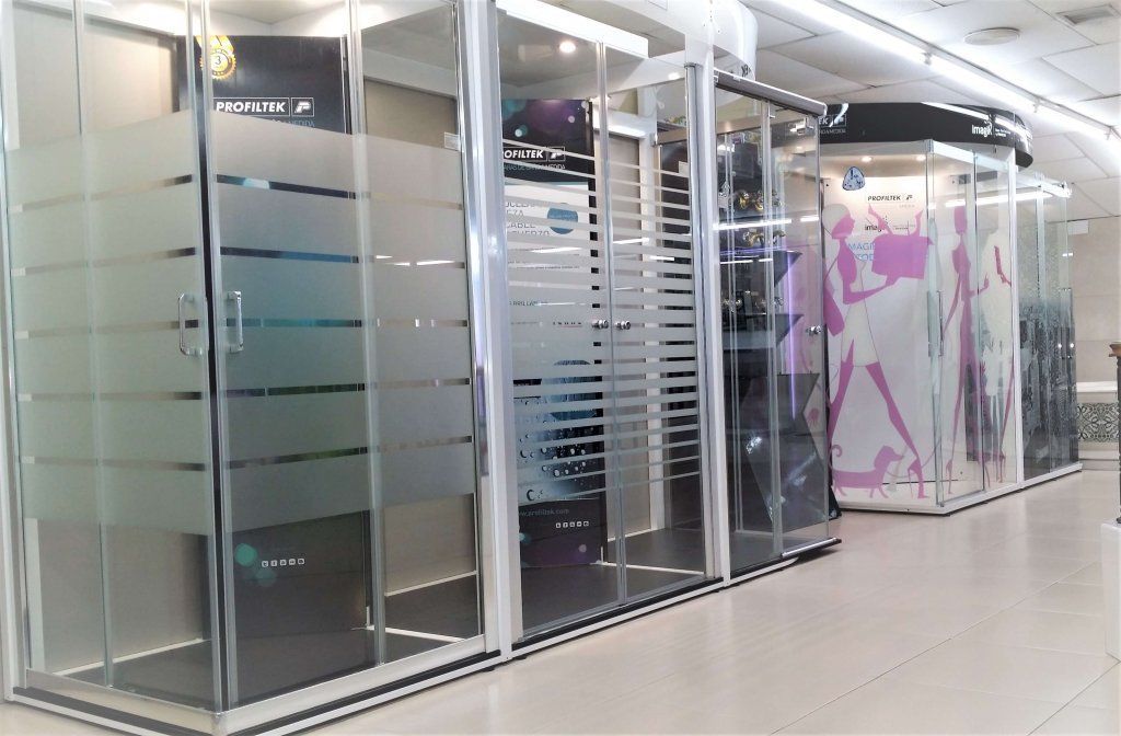 Cabinas de ducha en exhibición en una tienda; puertas de vidrio con diseño de rayas esmeriladas.