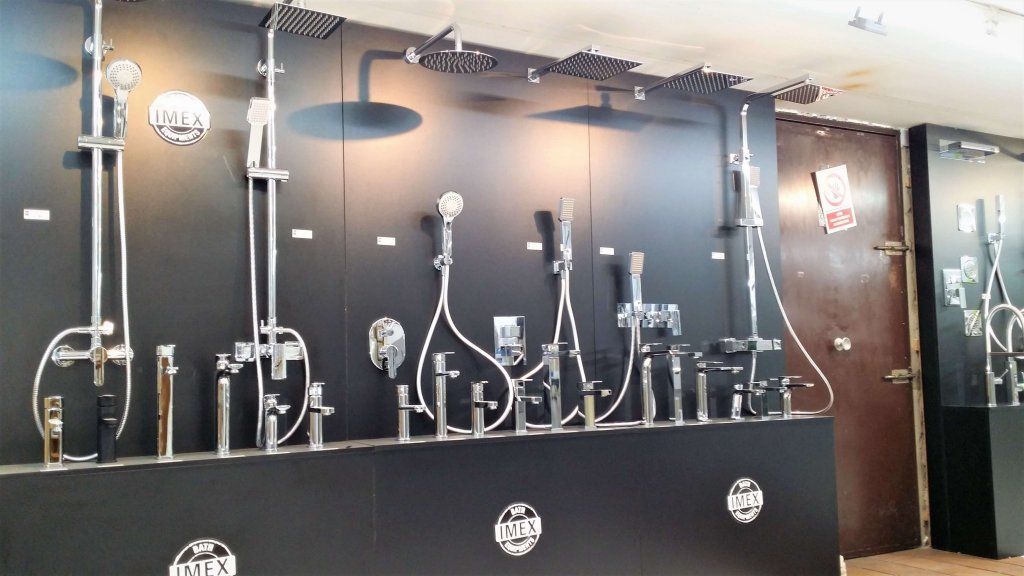 Exhibición de accesorios de baño: cabezales de ducha, grifos y controles montados en una pared negra en una sala de exposición.