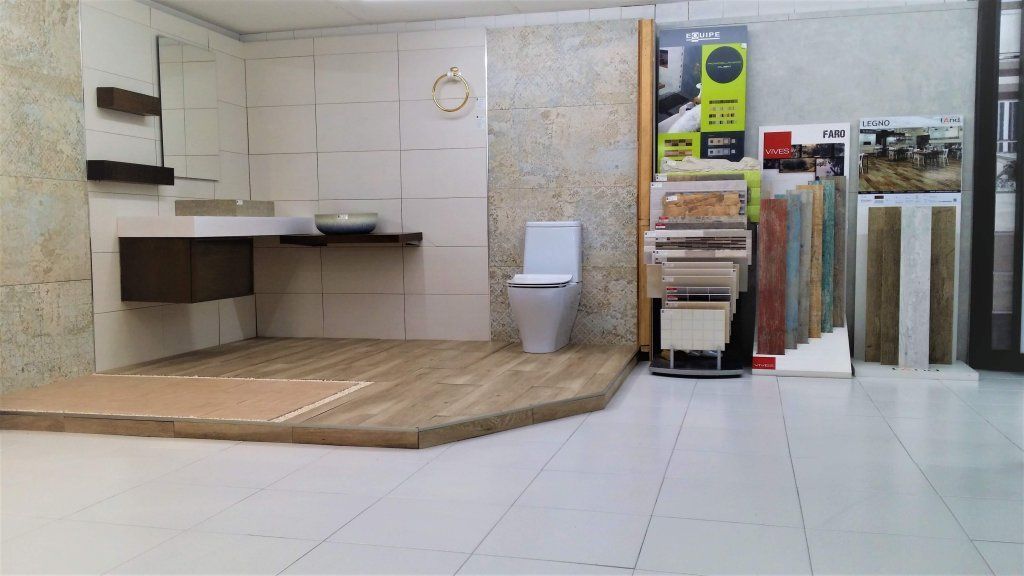 Exhibición de baño con muestras de madera y azulejos, inodoro, lavabo y estantes.