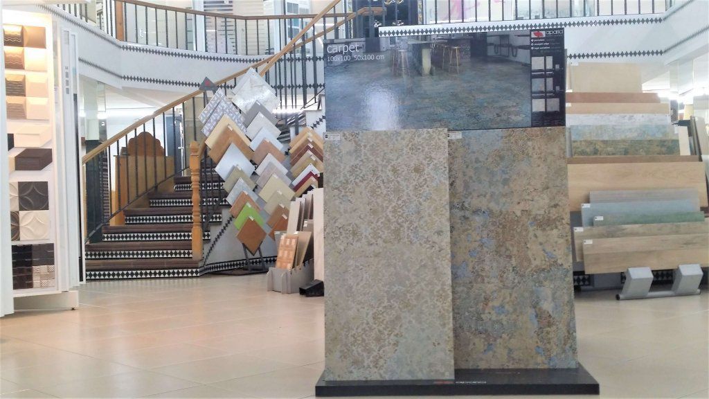 Interior de sala de exposición de azulejos con muestras de azulejos y escalera al fondo.