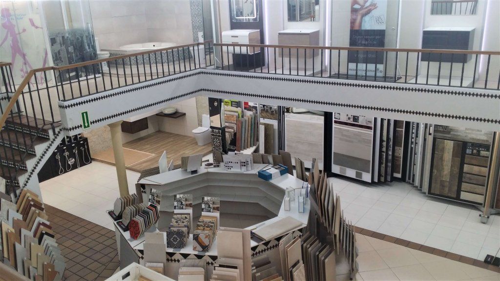 Una sala de exposición de azulejos con un diseño de dos pisos, que cuenta con varias exhibiciones de azulejos y un mostrador central.