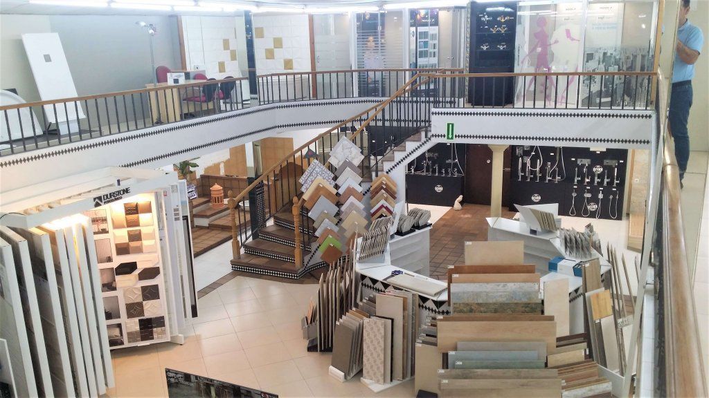 Sala de exposición de azulejos de dos pisos con varias muestras de azulejos expuestas; una persona se encuentra en el nivel superior, observando la tienda.