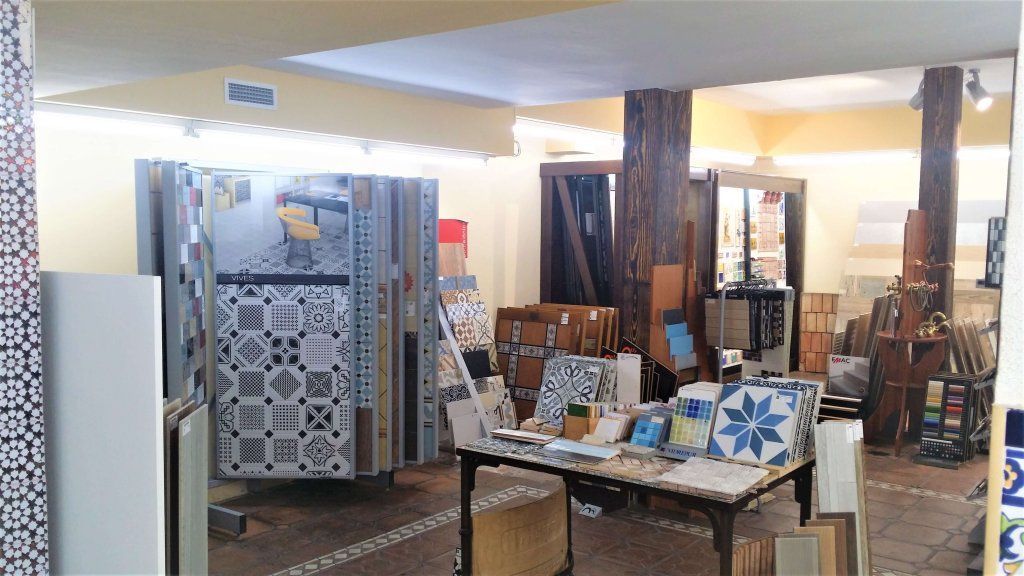 Interior de sala de exposición de azulejos con exhibidores de azulejos, muestras y un tronco de árbol central.