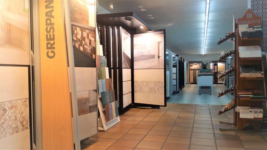 Interior de sala de exposición de azulejos con varias exhibiciones de azulejos a lo largo de las paredes y un pasillo central.