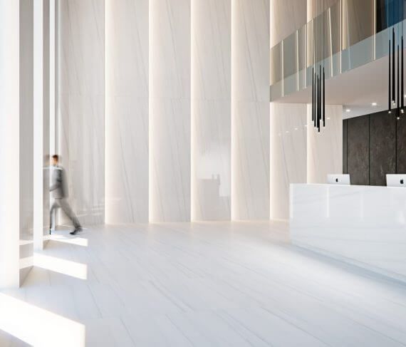 Vestíbulo moderno y blanco con una persona caminando entre columnas. Mostrador de recepción visible.