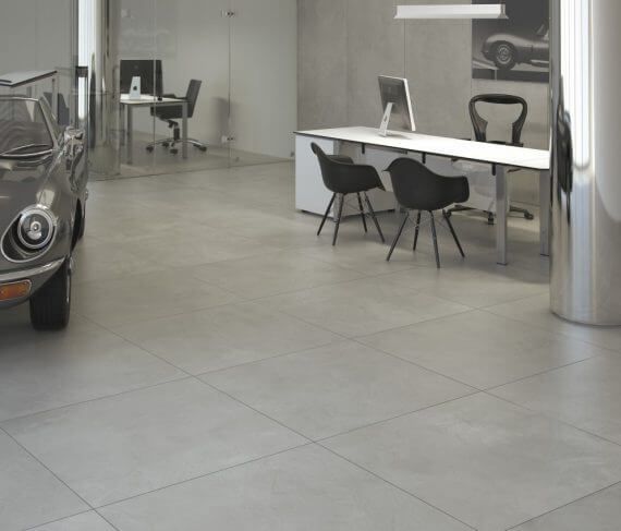 Suelo de baldosas grises de una moderna sala de exposición de coches con un coche clásico y escritorios con pantallas de ordenador.