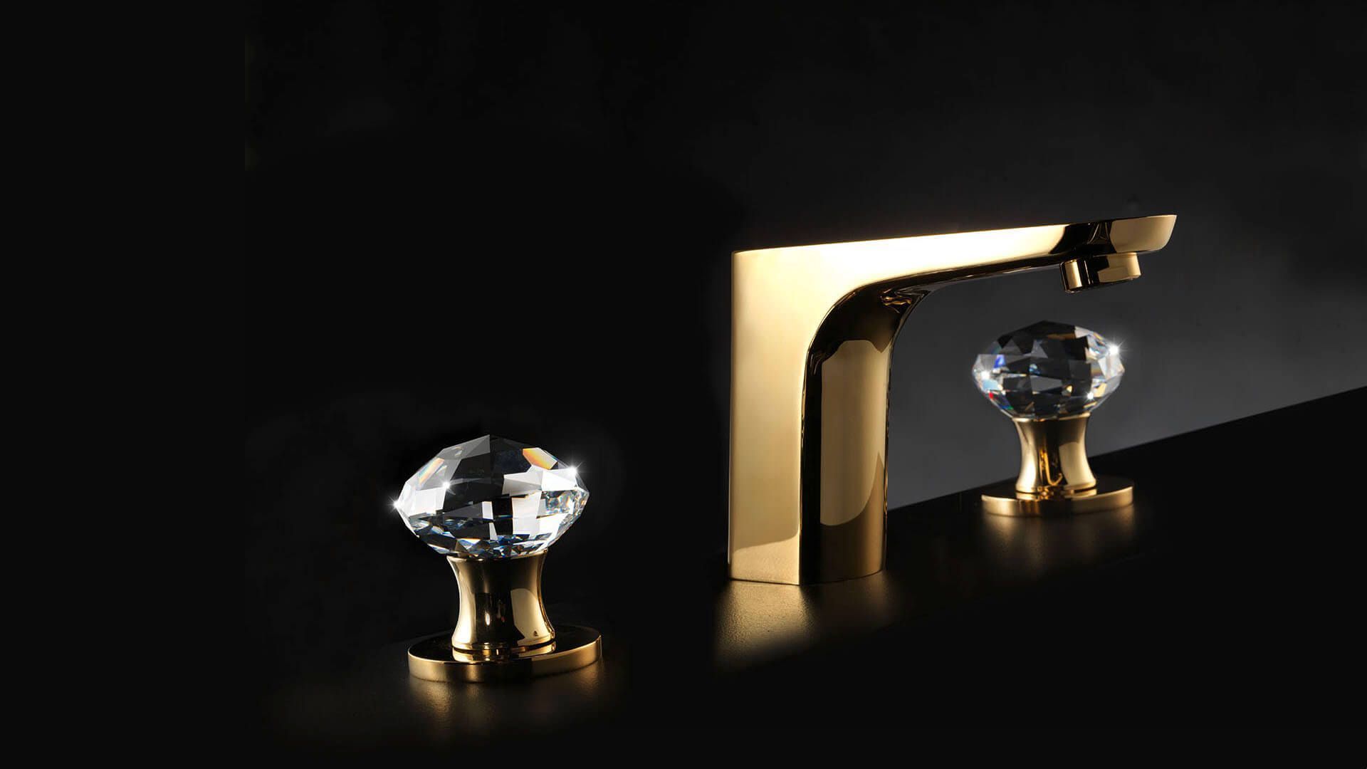 Grifo de baño dorado con pomos de cristal sobre superficie oscura.