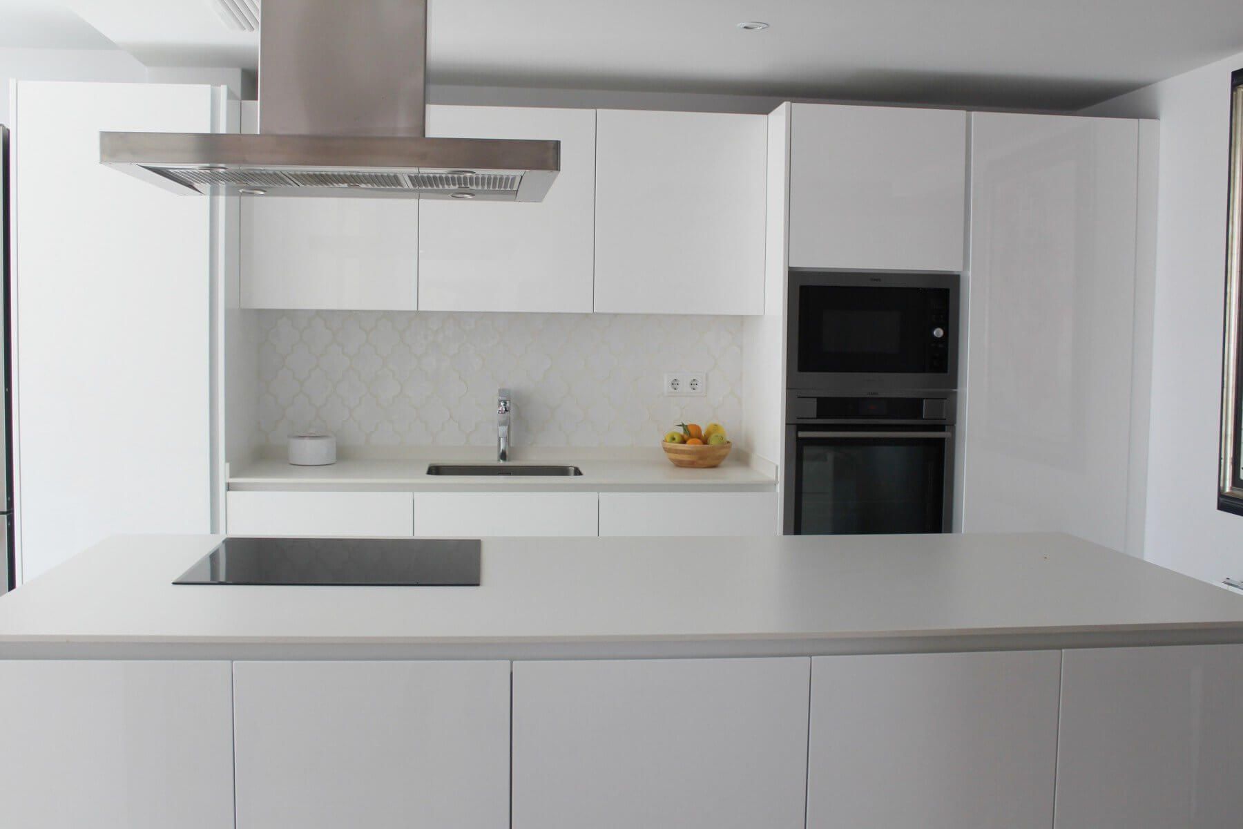 Cocina blanca moderna con isla, campana extractora de acero inoxidable, horno empotrado y anafe.