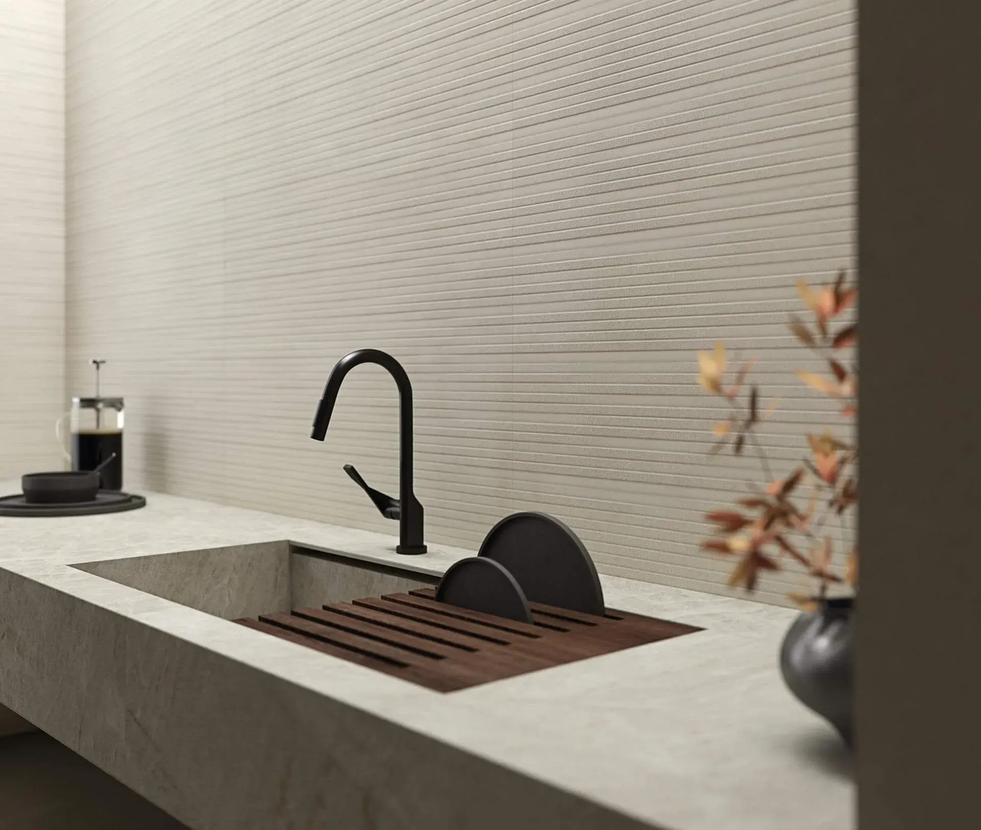 Fregadero de cocina con grifo negro, encimera de piedra clara, pared texturizada, prensa de café y jarrón.