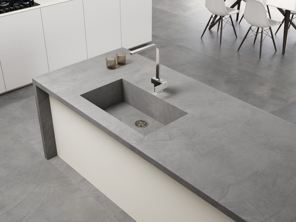 Isla de cocina de hormigón gris con fregadero rectangular incorporado, grifo cromado y gabinetes blancos.