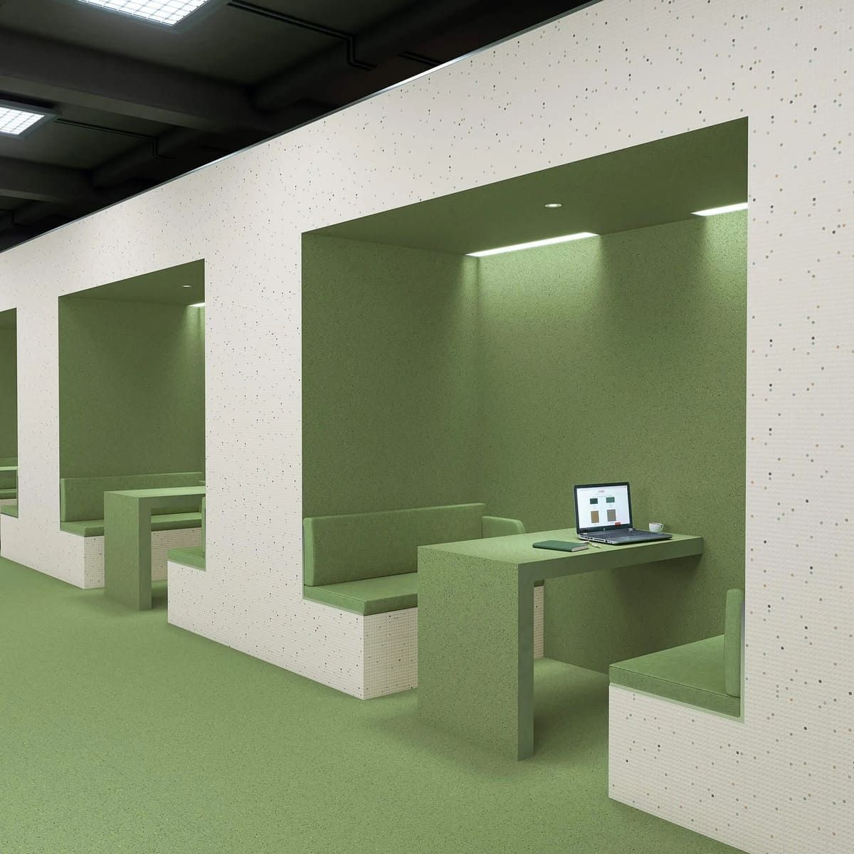 Cubículos verdes y blancos en una oficina. Uno de ellos tiene una computadora portátil sobre un escritorio.