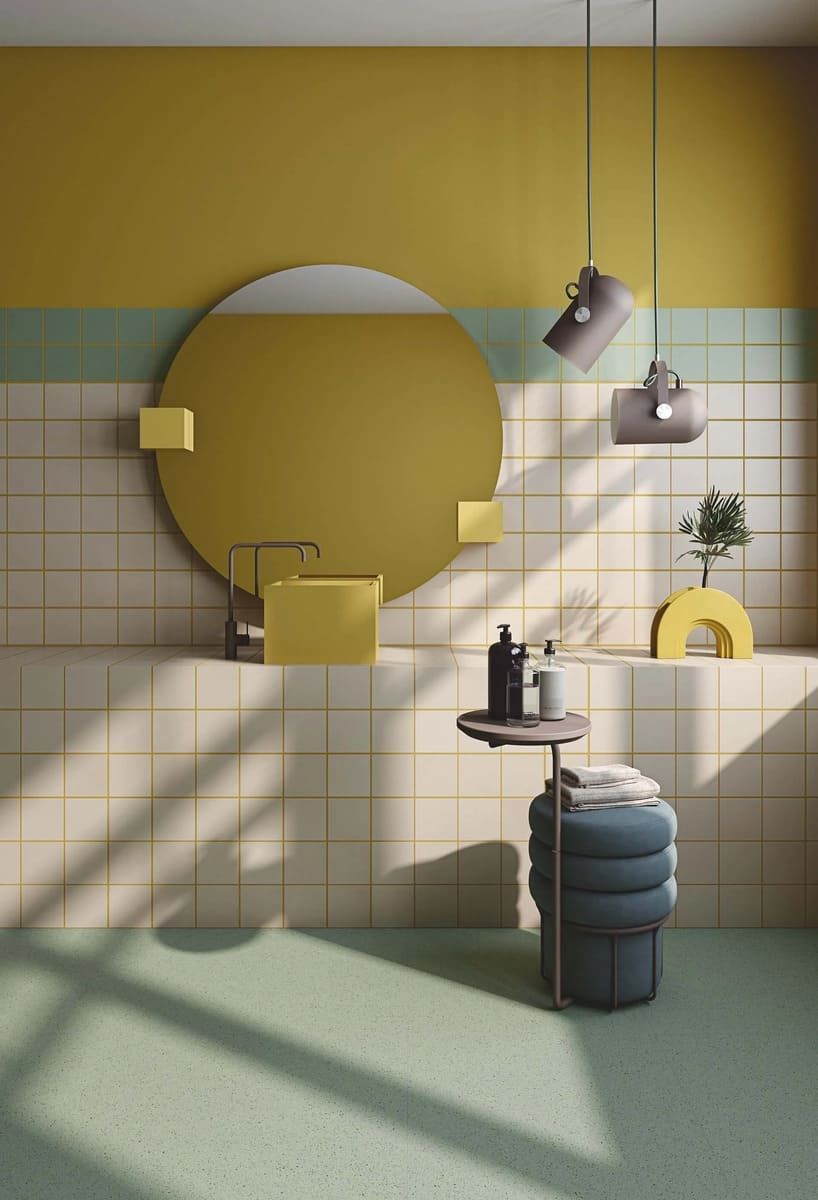 Baño con combinación de colores amarillo, verde y crema. Espejo redondo, lámparas colgantes y taburete decorativo.