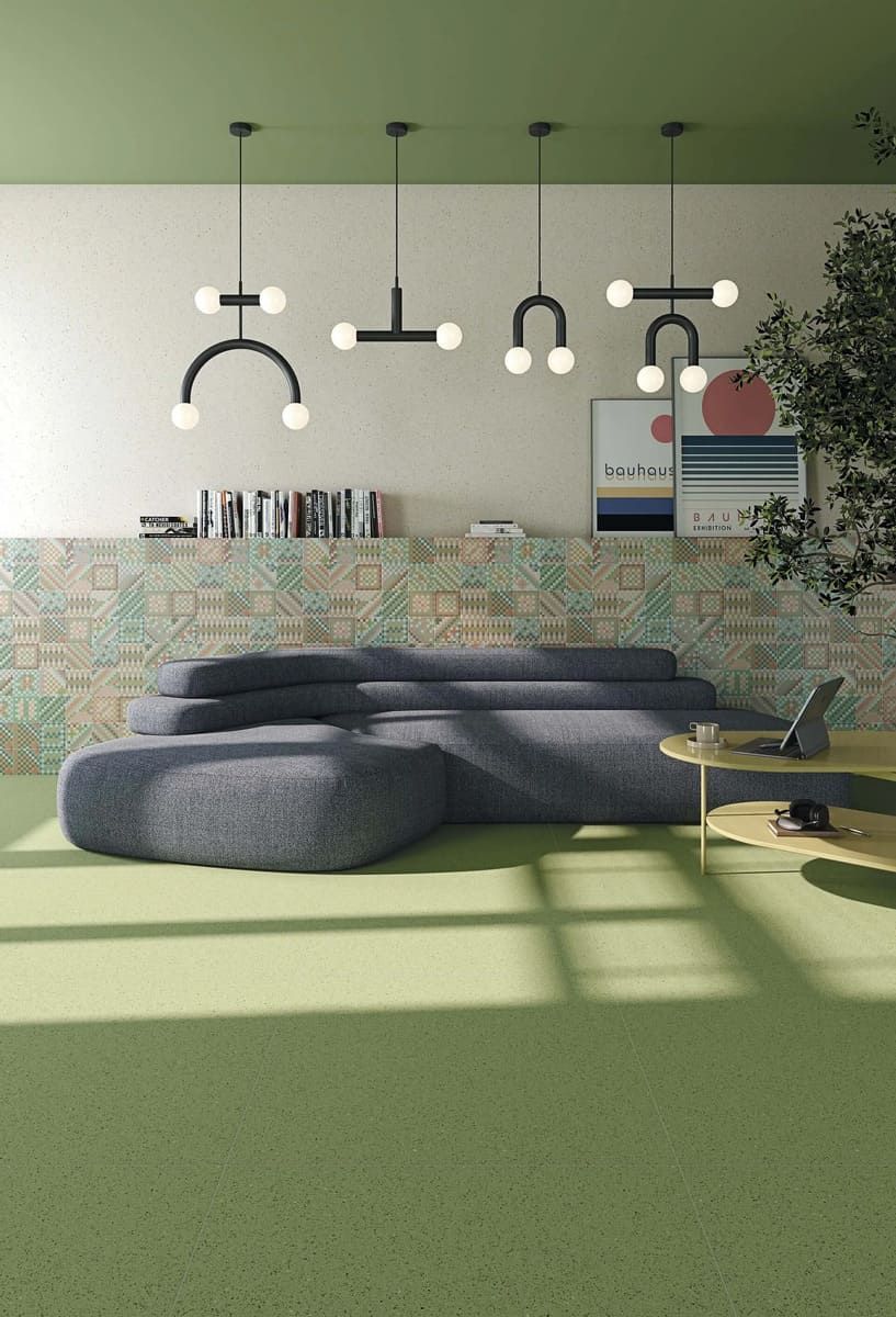 Sala de estar con un gran sofá azul, alfombra verde, pared estampada y lámparas colgantes modernas.