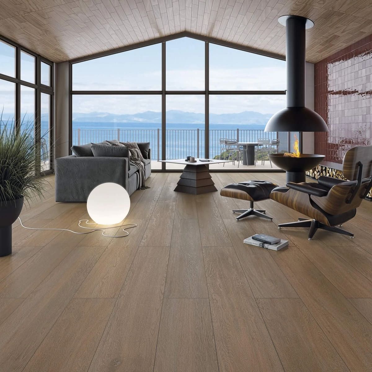 Sala de estar con pisos de madera, grandes ventanales con vista al agua, chimenea y muebles modernos.