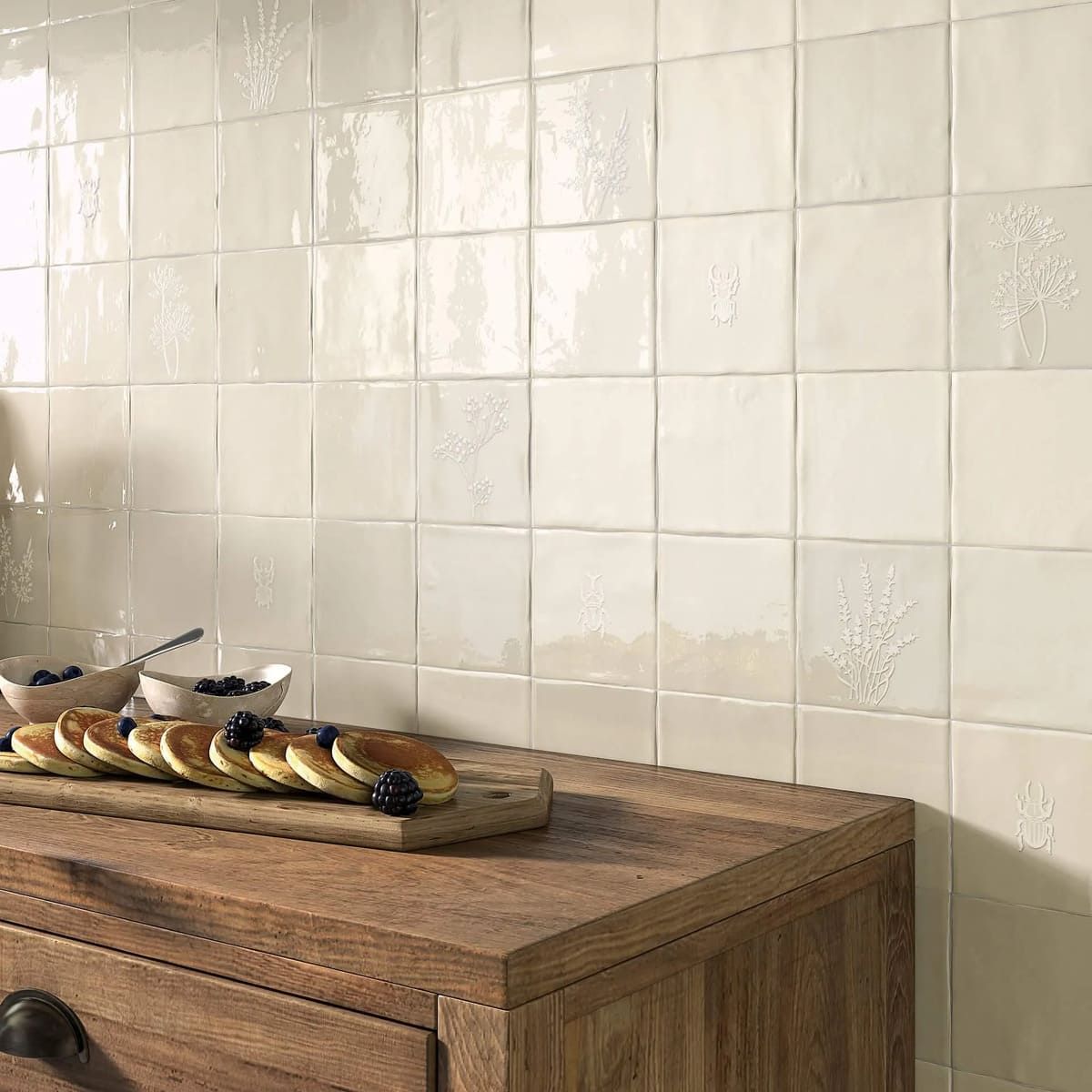 Azulejos cuadrados de color crema en una pared detrás de una encimera de madera con panqueques y arándanos.
