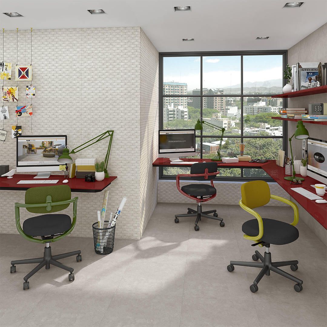 Espacio de oficina con escritorios y sillas coloridas. Gran ventanal con vista a la ciudad y estanterías rojas.